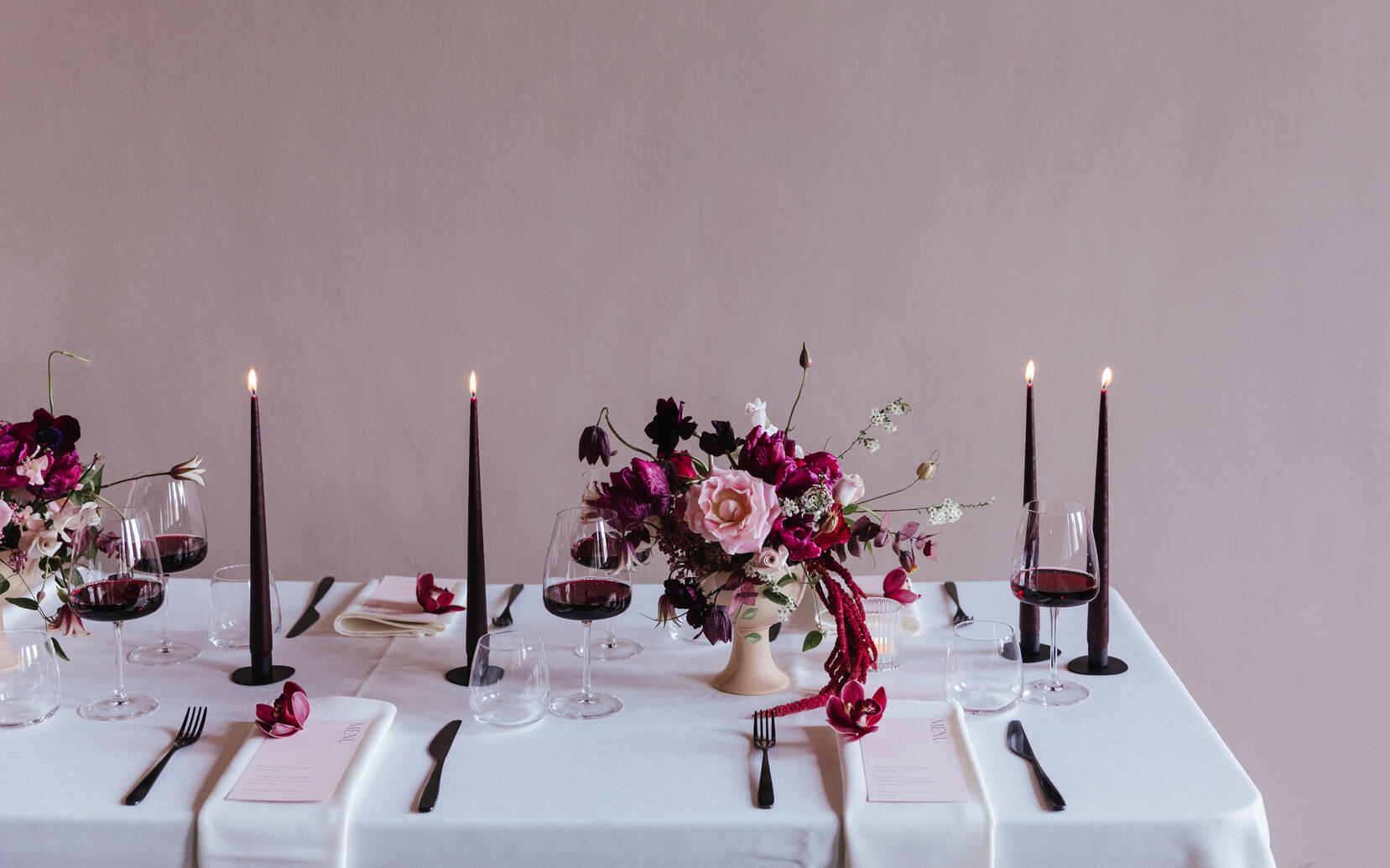 Dining table with pink flowers, purple dinner candles, stationery and glasses of red wine