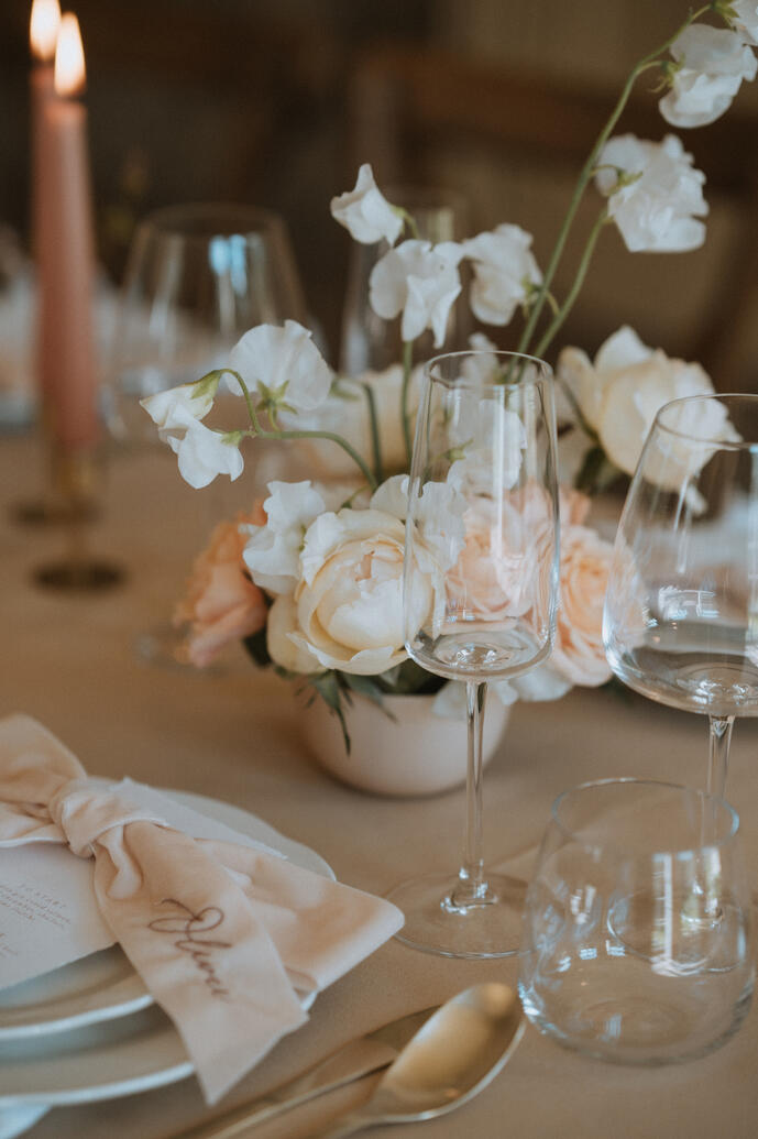 A bowl of flowers on a wedding table alongside gold cutlery and embroidered bows