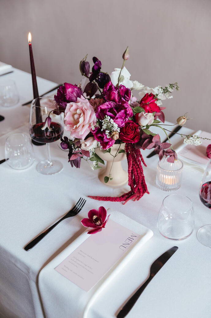 Dining table with pink flowers, purple dinner candles, stationery and glasses of red wine